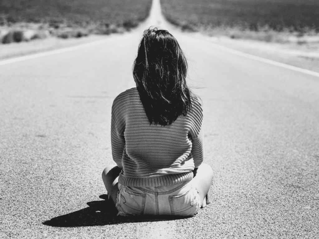 Woman sitting in the middle of a long road with her back to the camera